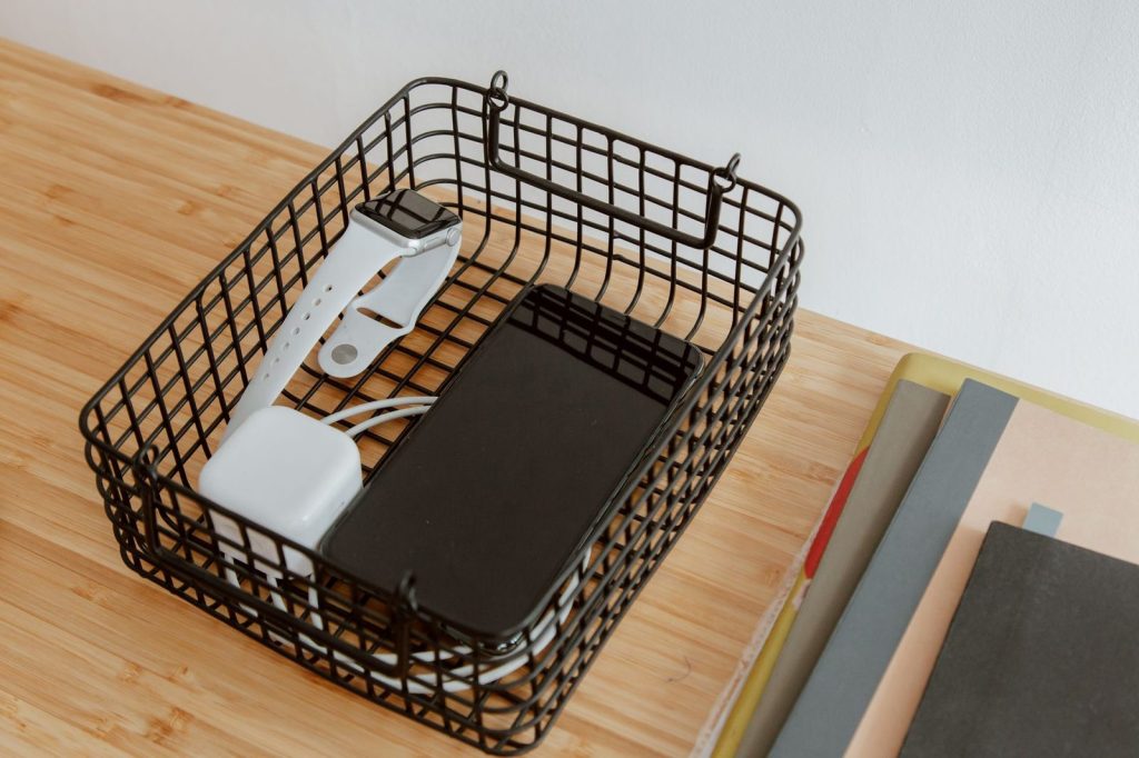 Phone and small gadgets charging in a wire basket on a wooden desk