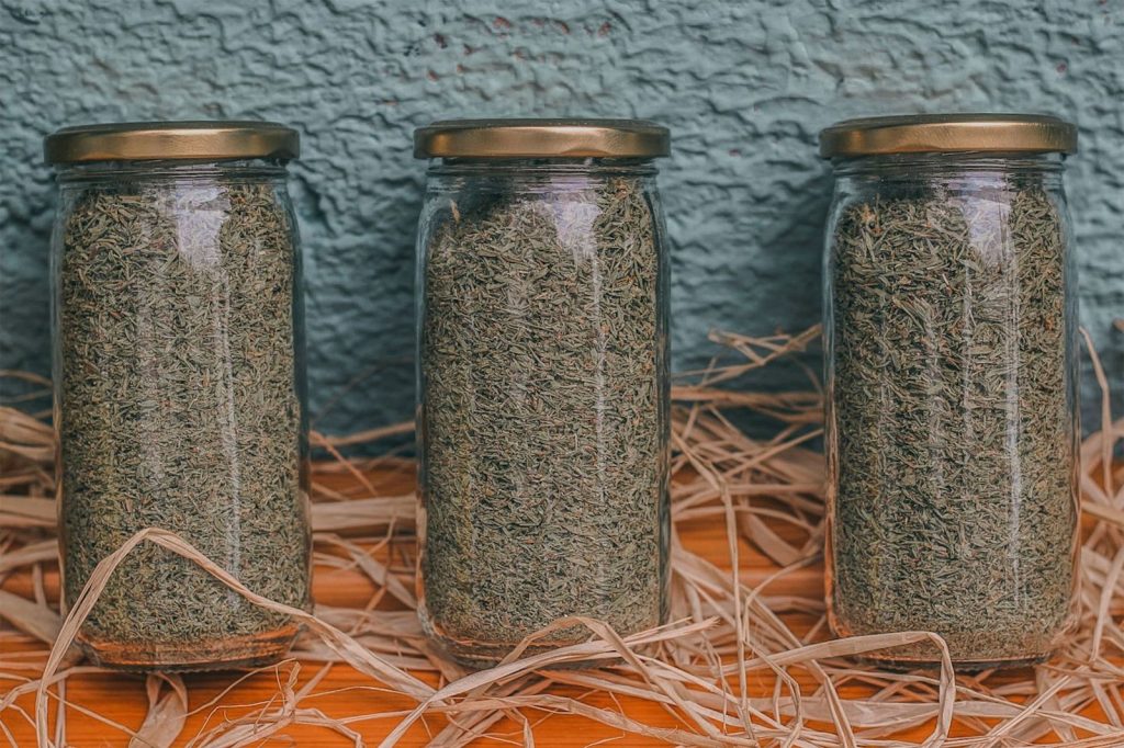 Three glass jars of dried herbs on a rustic wooden surface